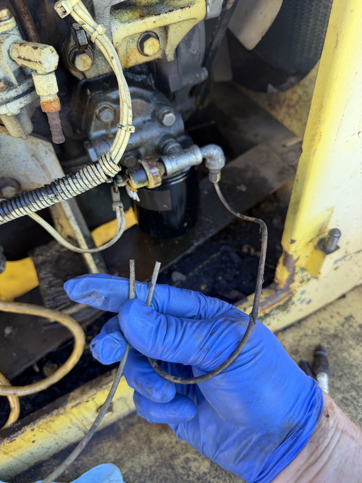 Gloved hand holding a broken small-bore steel line in front of the filter head