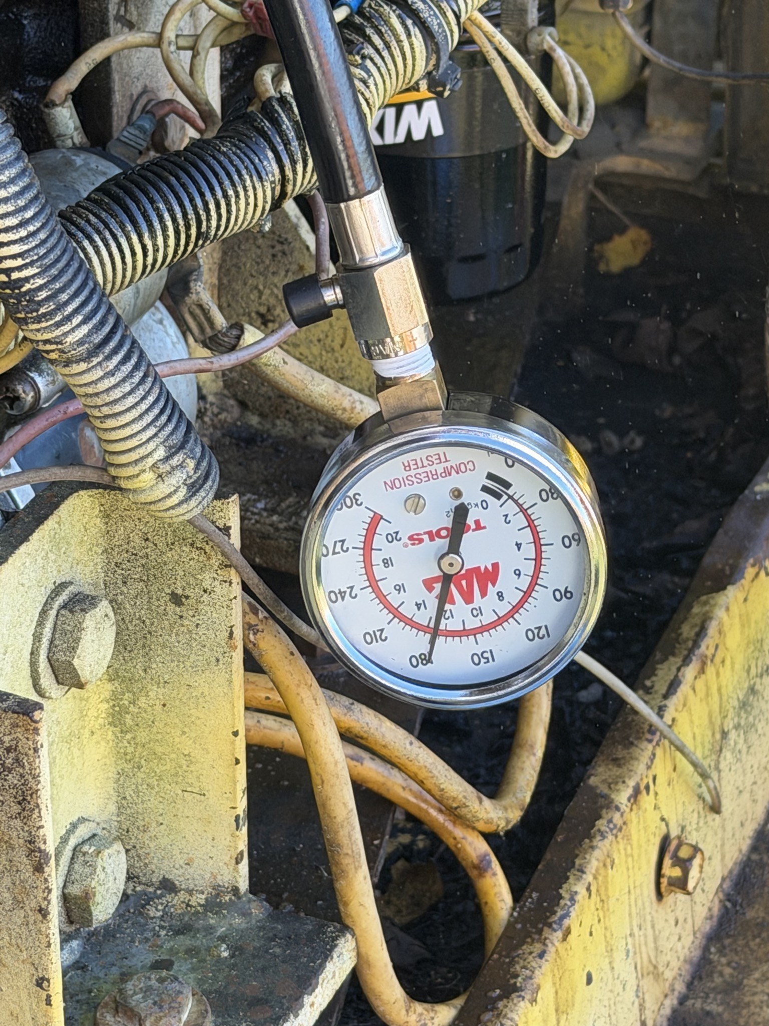 Compression tester off the engine and lying on the frame rail, dial upside down, pointer still on 180
